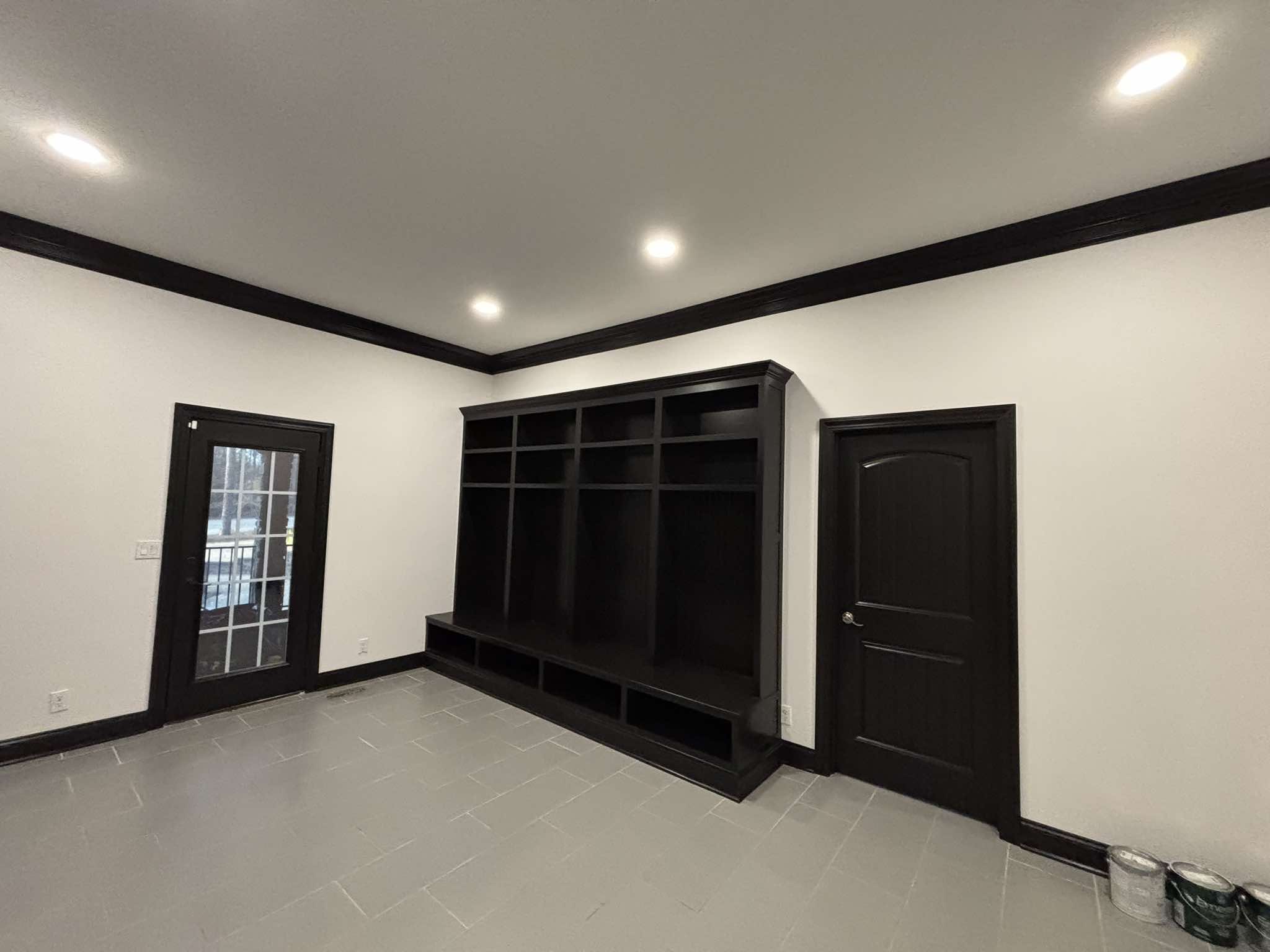 Finished room with a black built-in shelving unit, black door, dark crown molding, and white walls