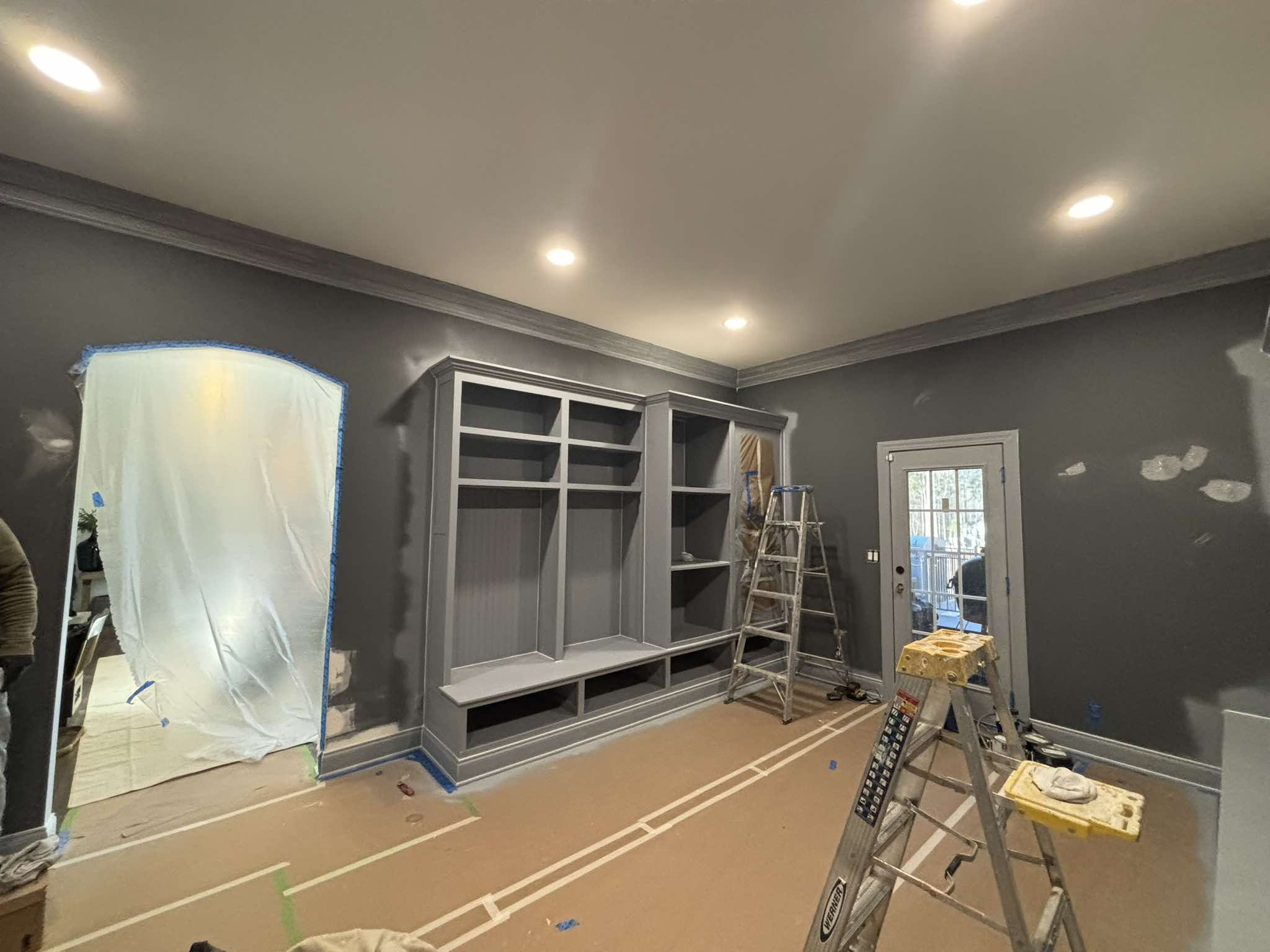 Built-in shelving and gray walls during interior preparation with floors and openings protected
