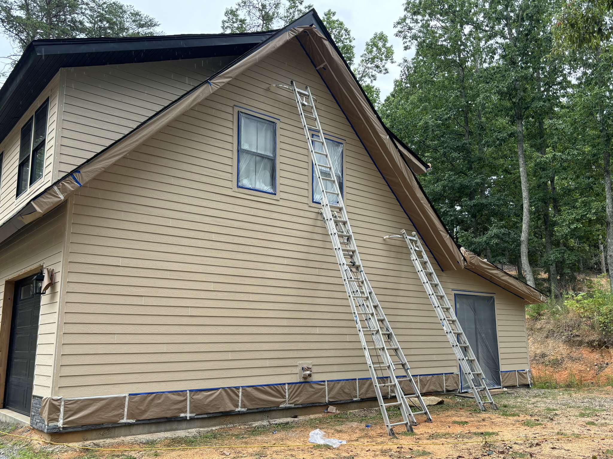 Garage side elevation before painting with tan siding and ladders at the upper story