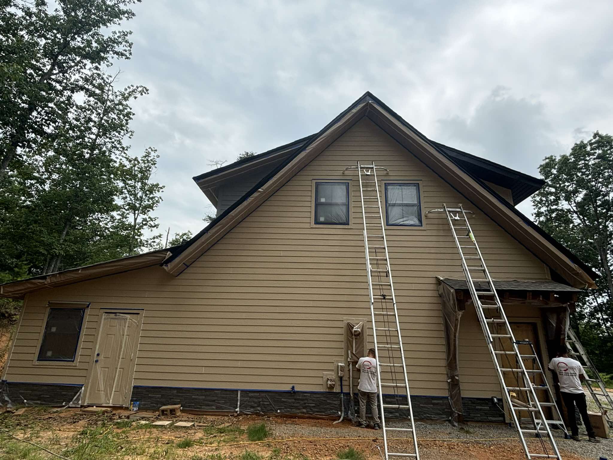 Exterior painting in progress on the tan rear garage wall with painters and ladders
