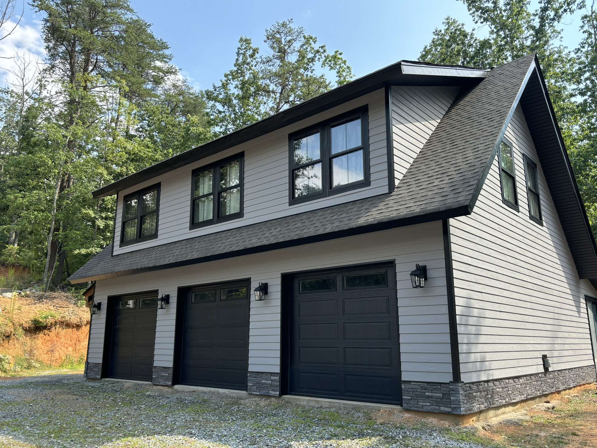 Completed three-car garage viewed at an angle with light gray siding and strong black trim