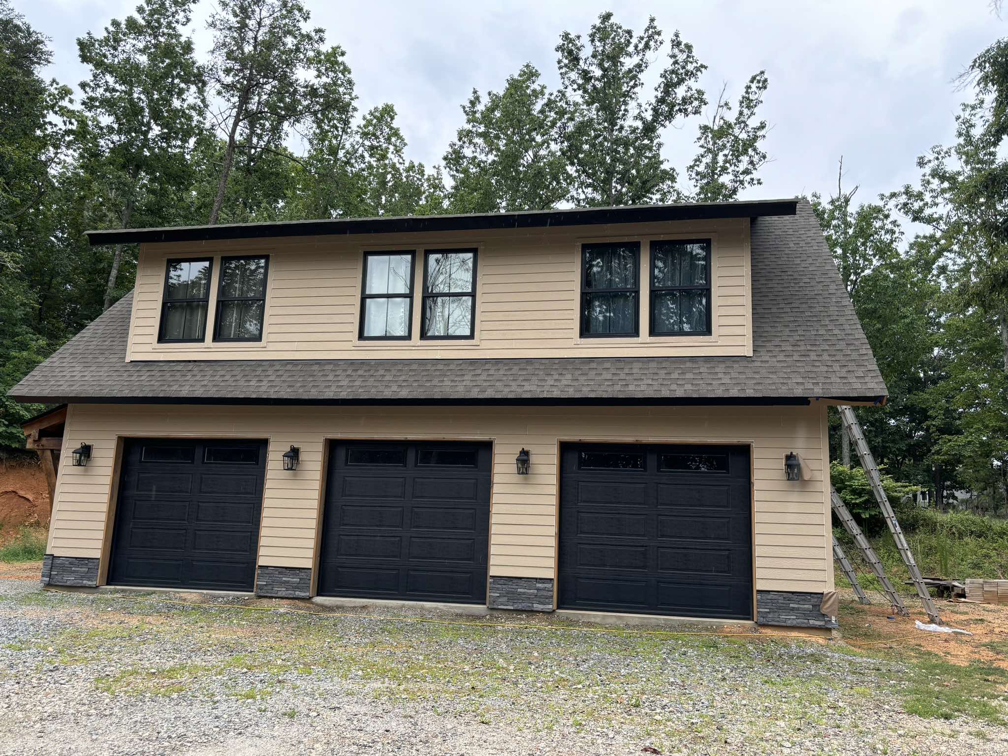 Front garage elevation before painting with tan siding and three dark doors