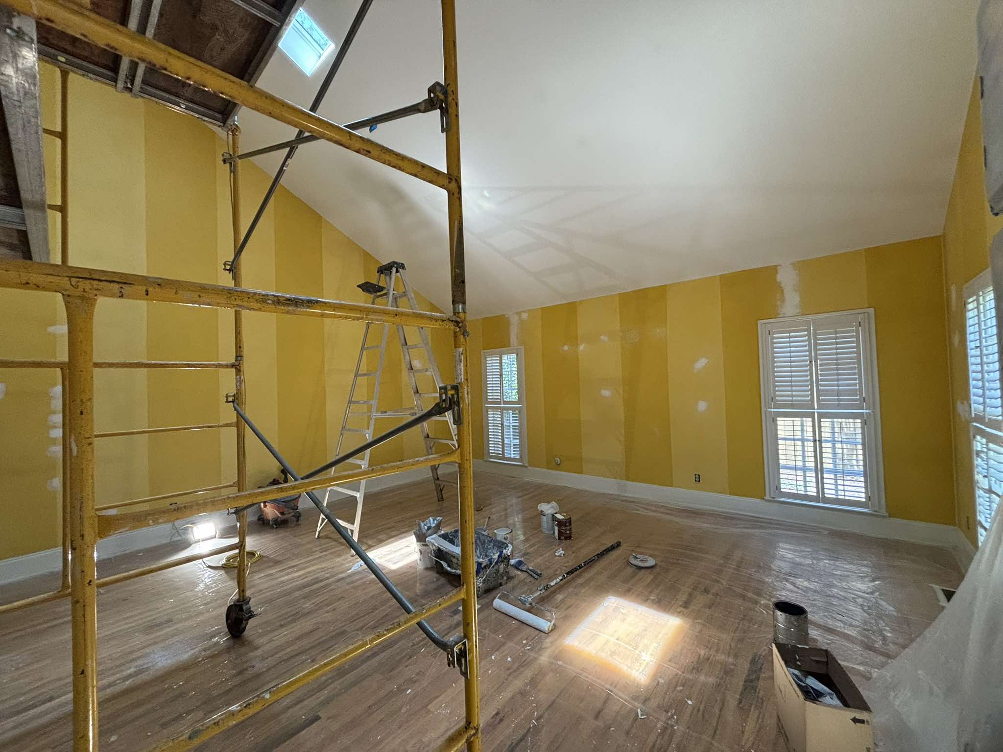 Interior painting in progress with scaffold positioned against the yellow walls below the high ceiling