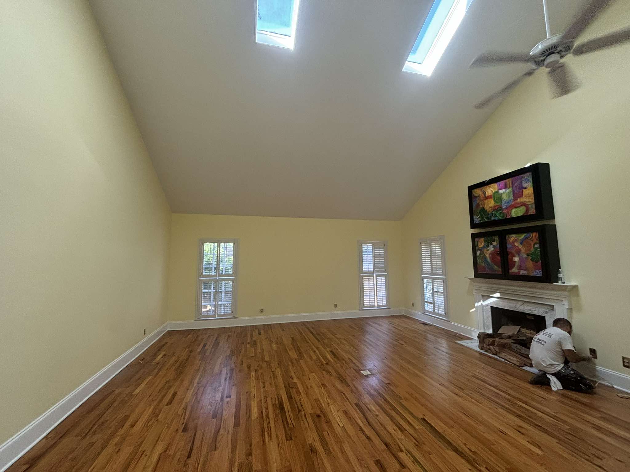 Finished high-ceiling living room with pale walls, white fireplace trim, and polished hardwood floors