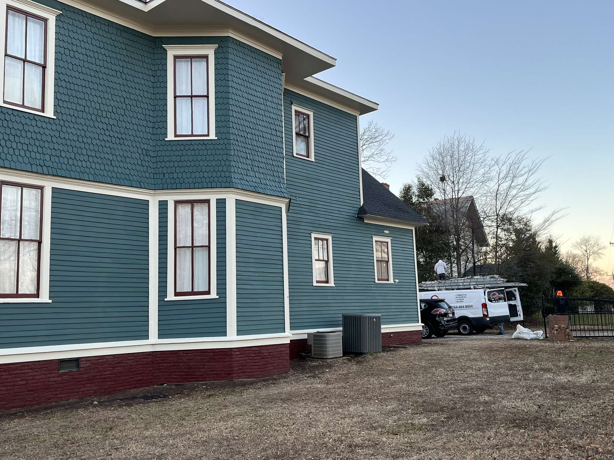 Finished side elevation of the historic home with teal siding, pale trim, tall windows, and a red masonry base