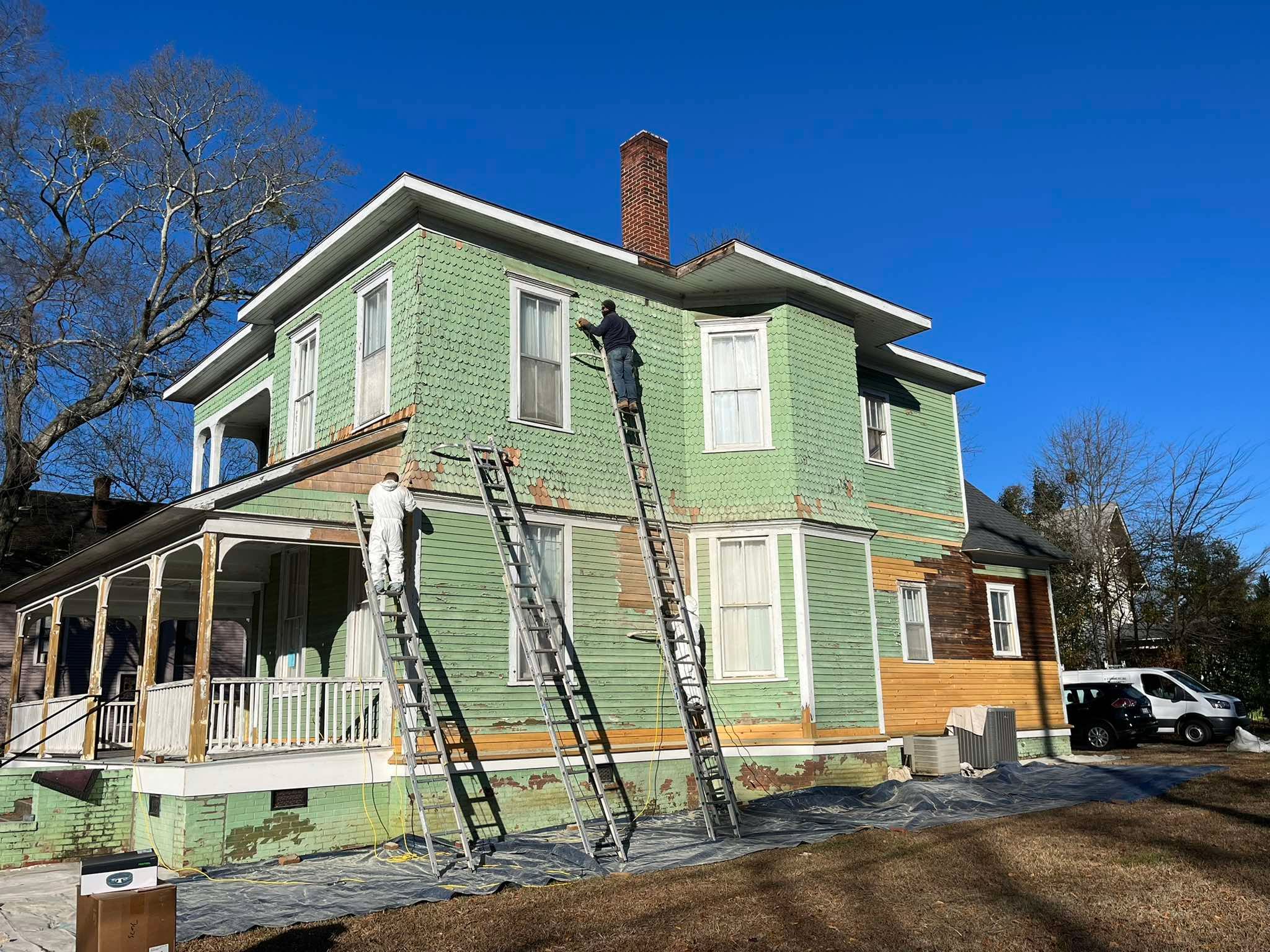 Painters working from ladders on the light green historic-home exterior and porch