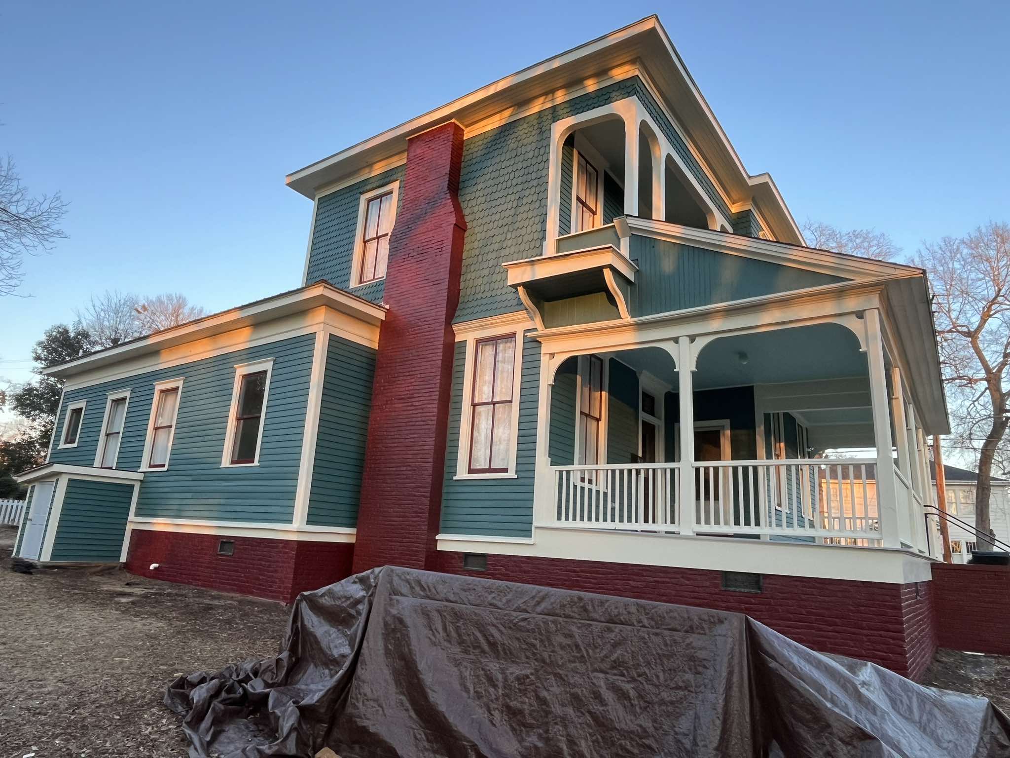 Finished rear and side elevations with teal siding, pale architectural trim, and a red masonry foundation