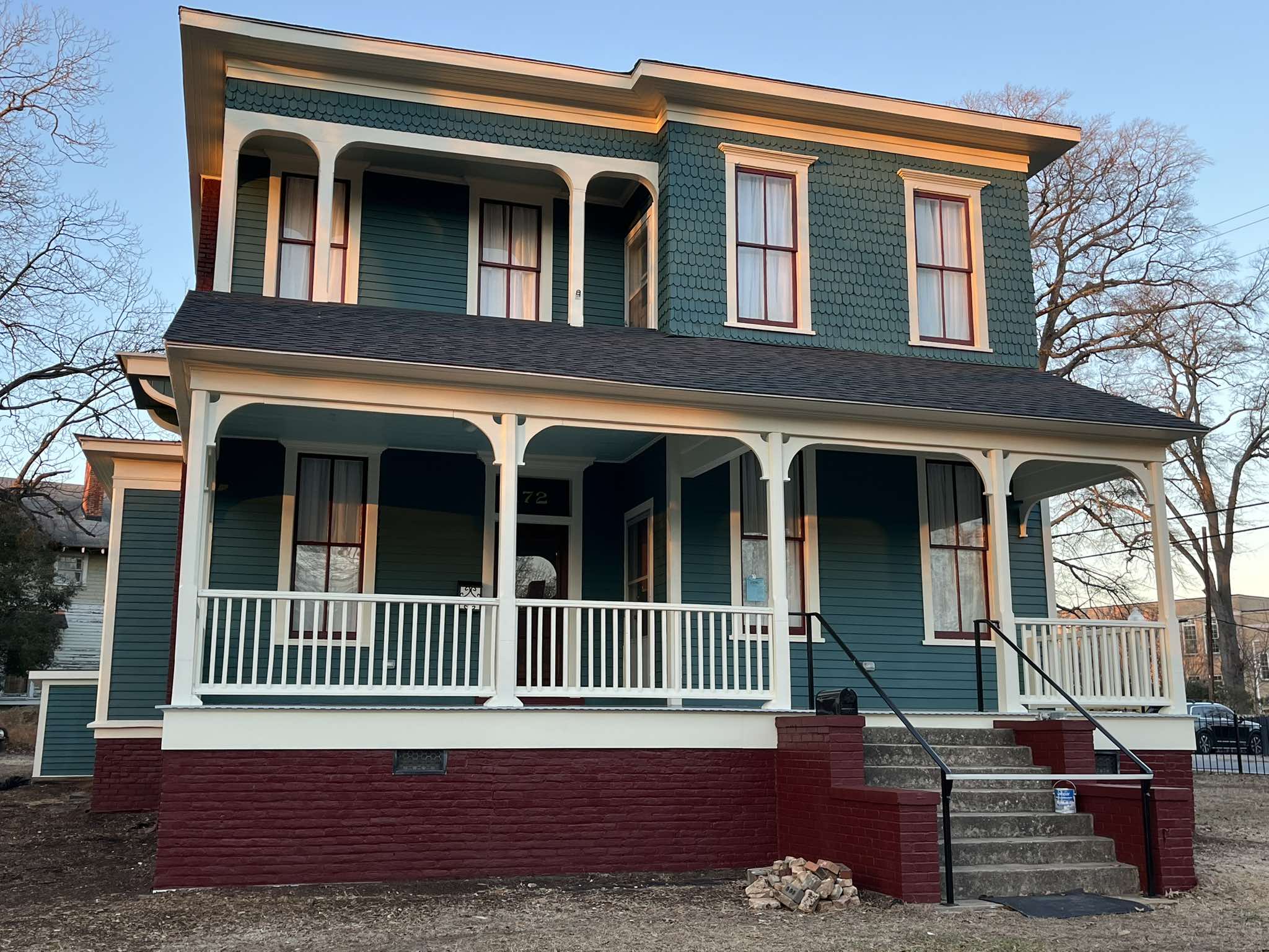 Completed front elevation with teal siding, white porch details, red window accents, and a red masonry base
