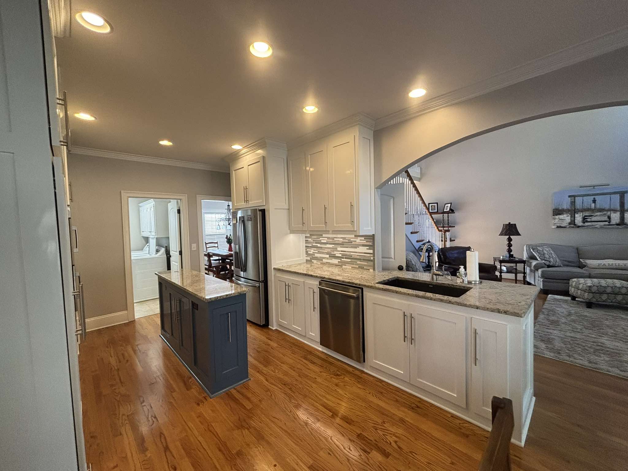 Finished kitchen with white painted cabinets, warm wood floors, and a contrasting dark island