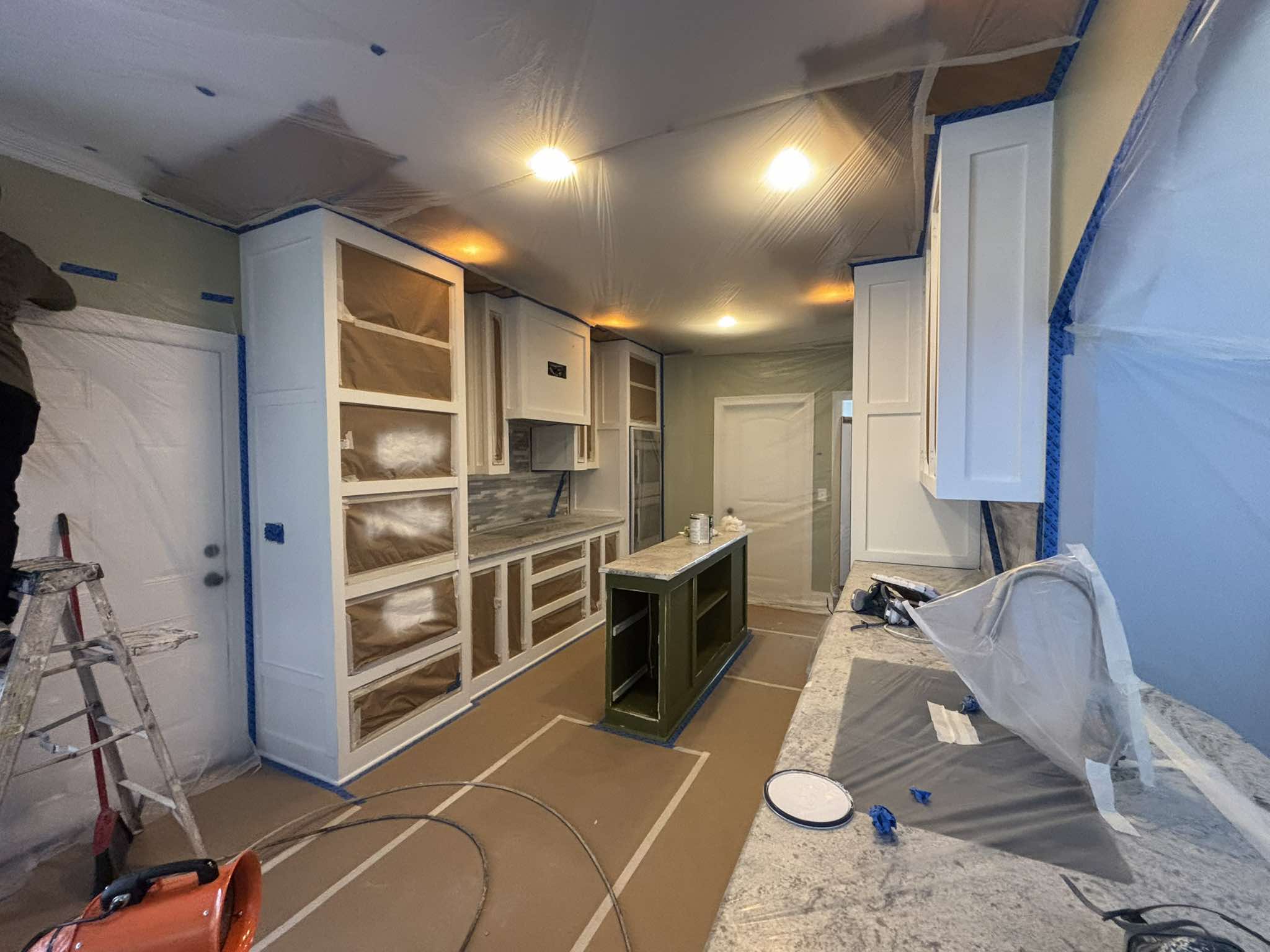 Kitchen during cabinet preparation with open shelving, protected surfaces, and ladders in the work area