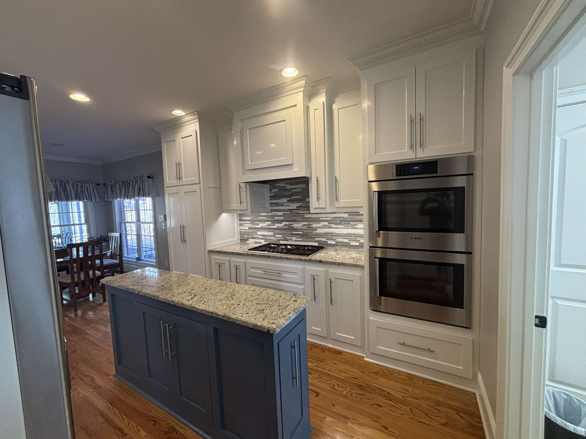 Wide finished view of white cabinetry, stainless appliances, patterned backsplash, and a dark island