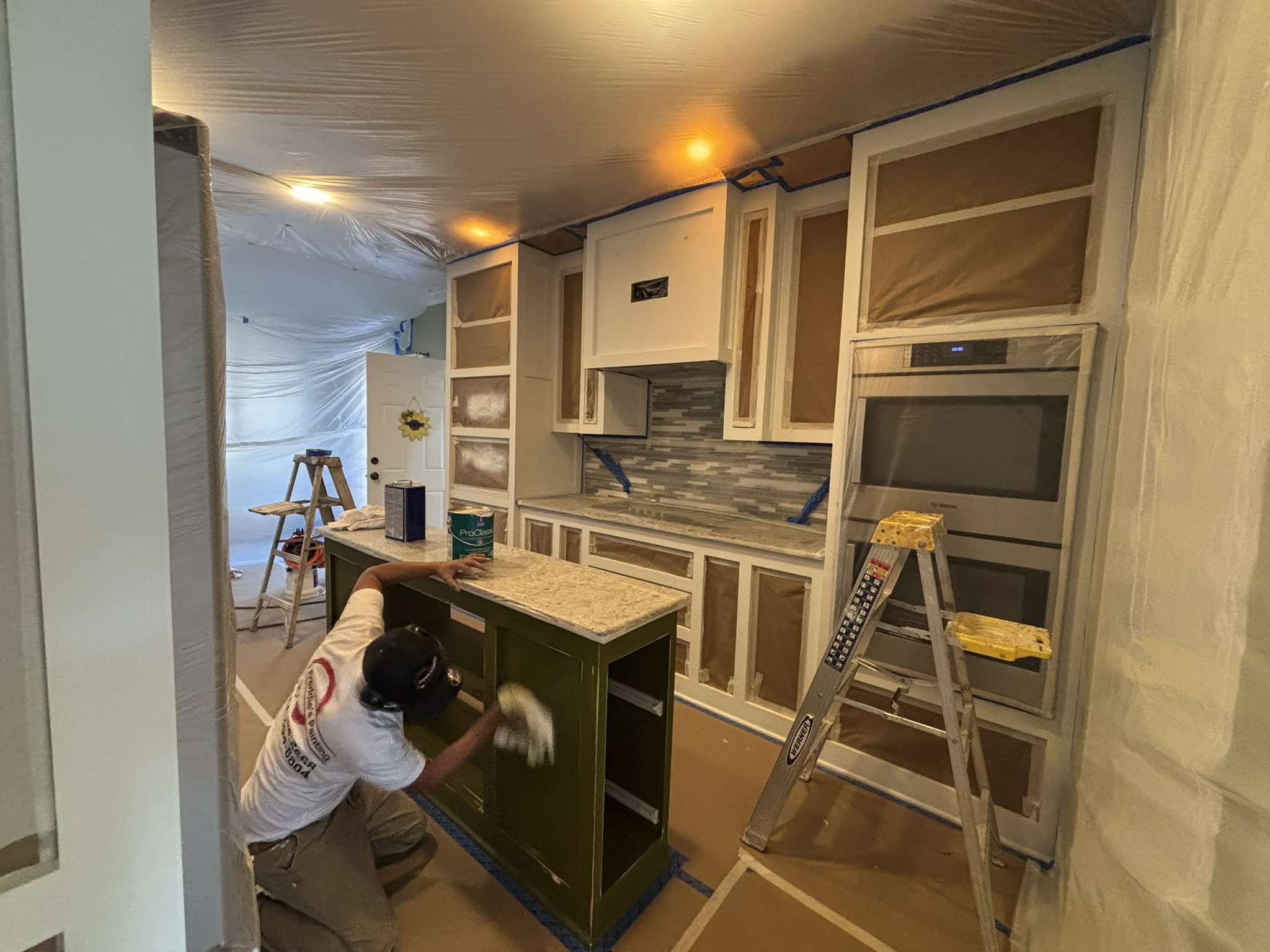 Painter working on the dark kitchen island while surrounding cabinetry and floors remain protected