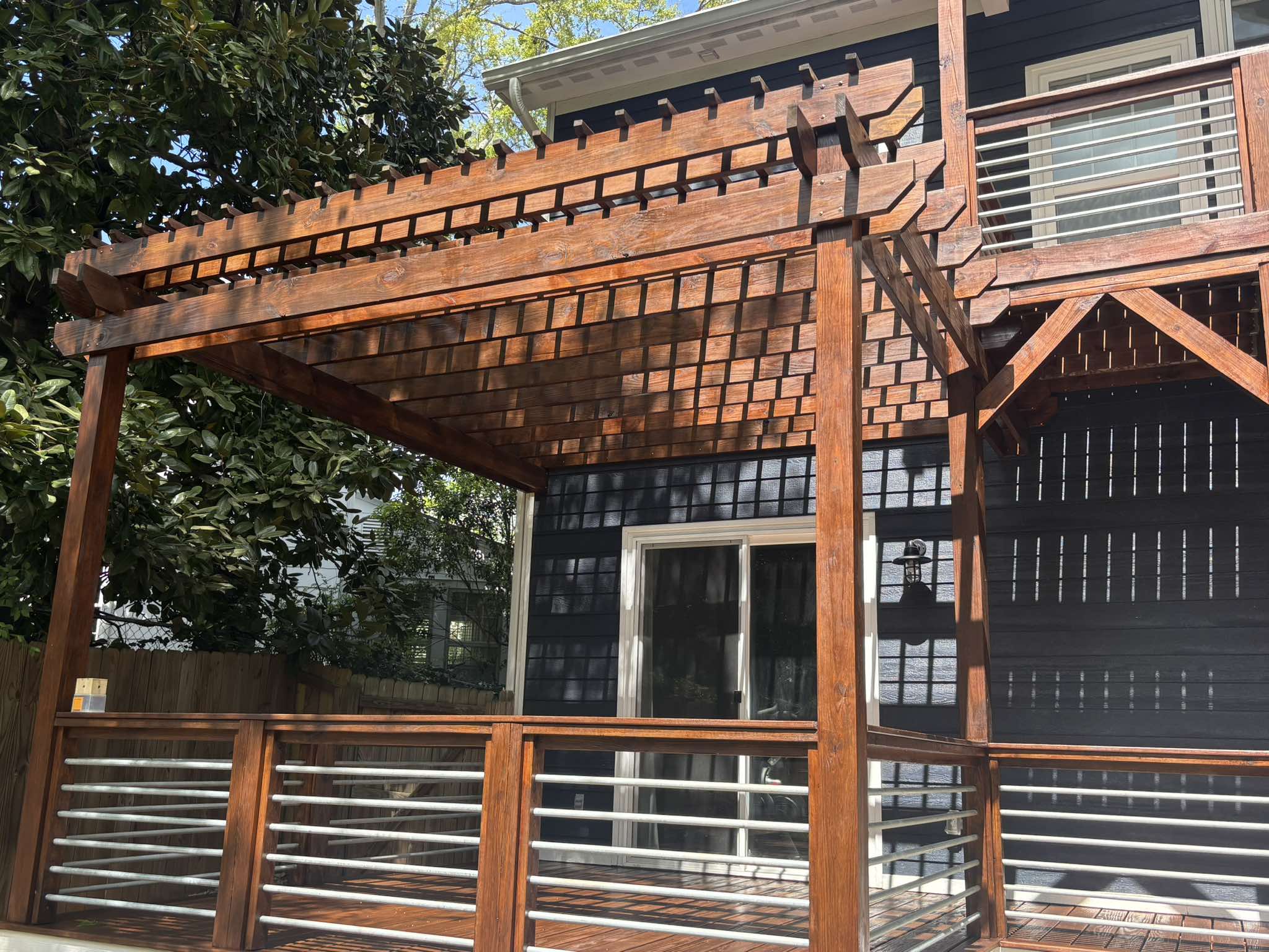 Finished stained pergola, deck railing, and geometric wood lattice against the dark home exterior