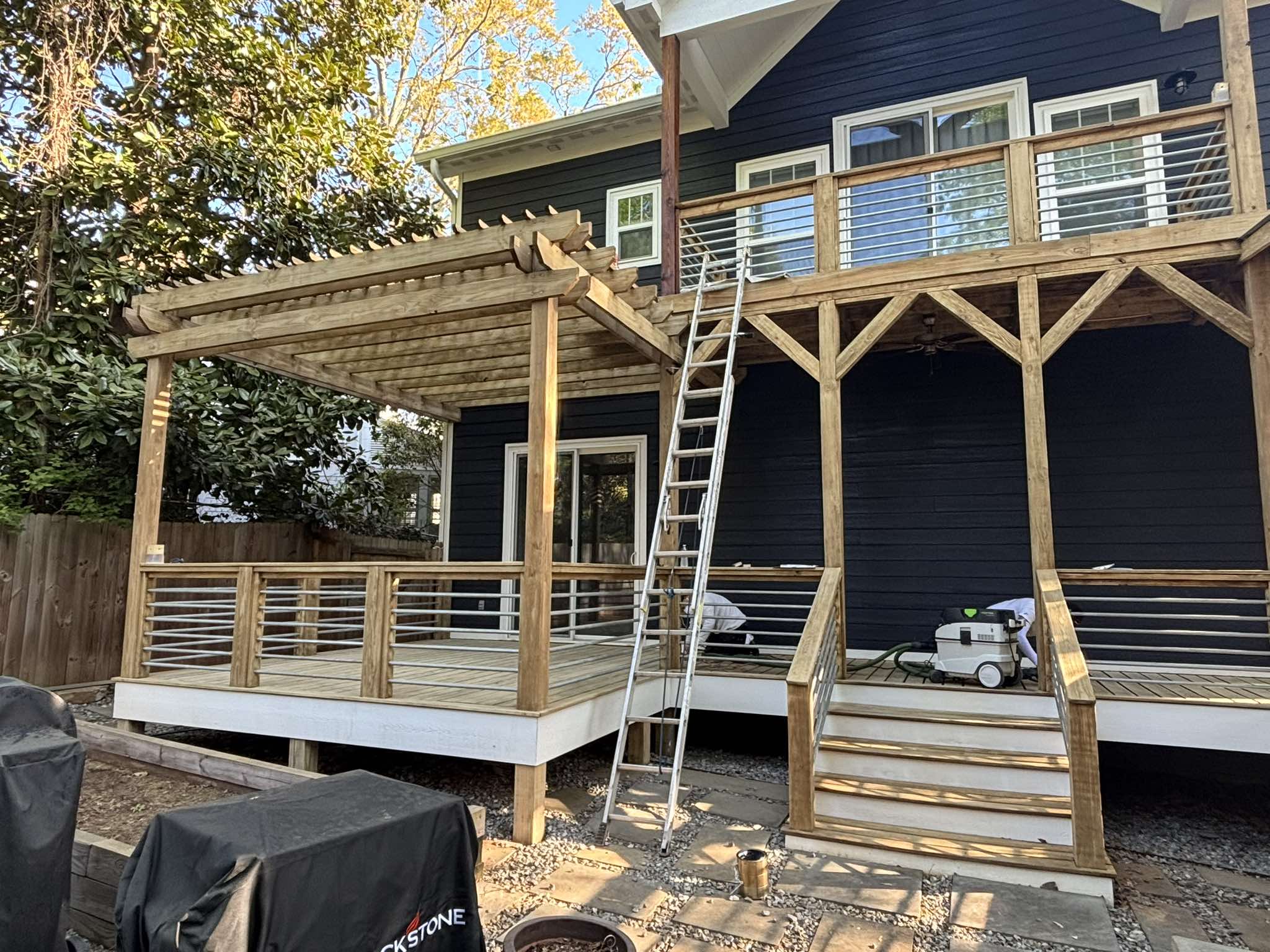 Unstained pergola and deck railing during preparation with a ladder positioned at the upper deck
