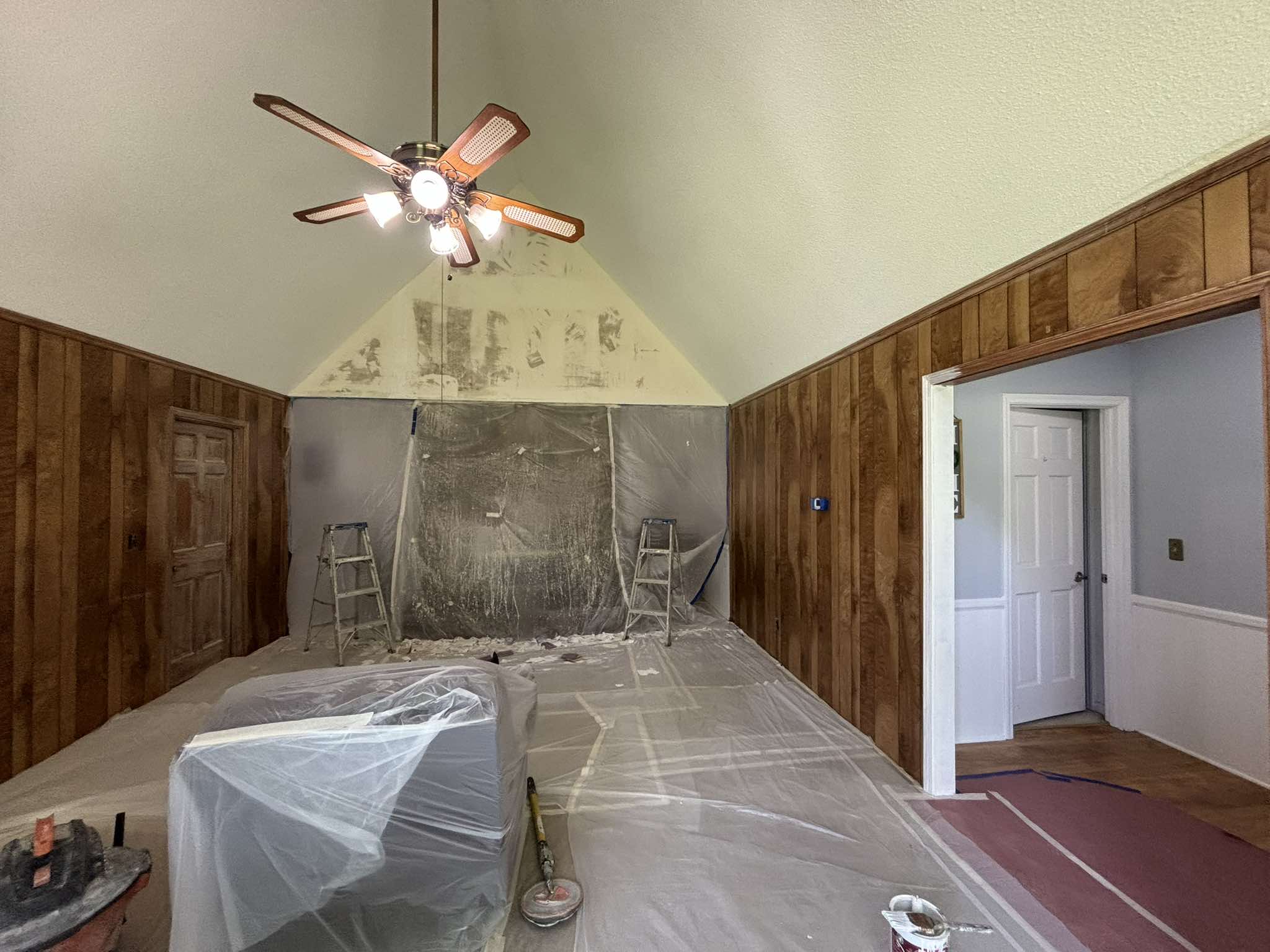 Interior preparation beneath the vaulted ceiling with covered furniture and patched wall sections
